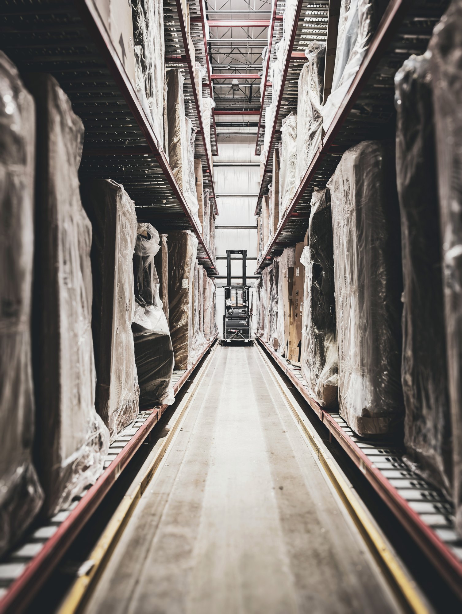 Forklift at the end of a long warehouse aisle lined with wrapped inventory